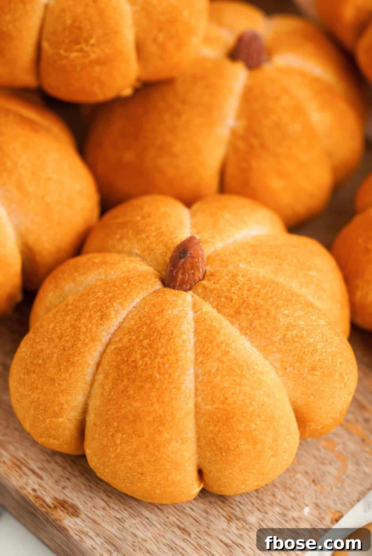 Spiced Pumpkin Feast Rolls 2 Close-up of golden-brown pumpkin-shaped dinner rolls on a rustic wooden cutting board, highlighting their perfect form and texture.