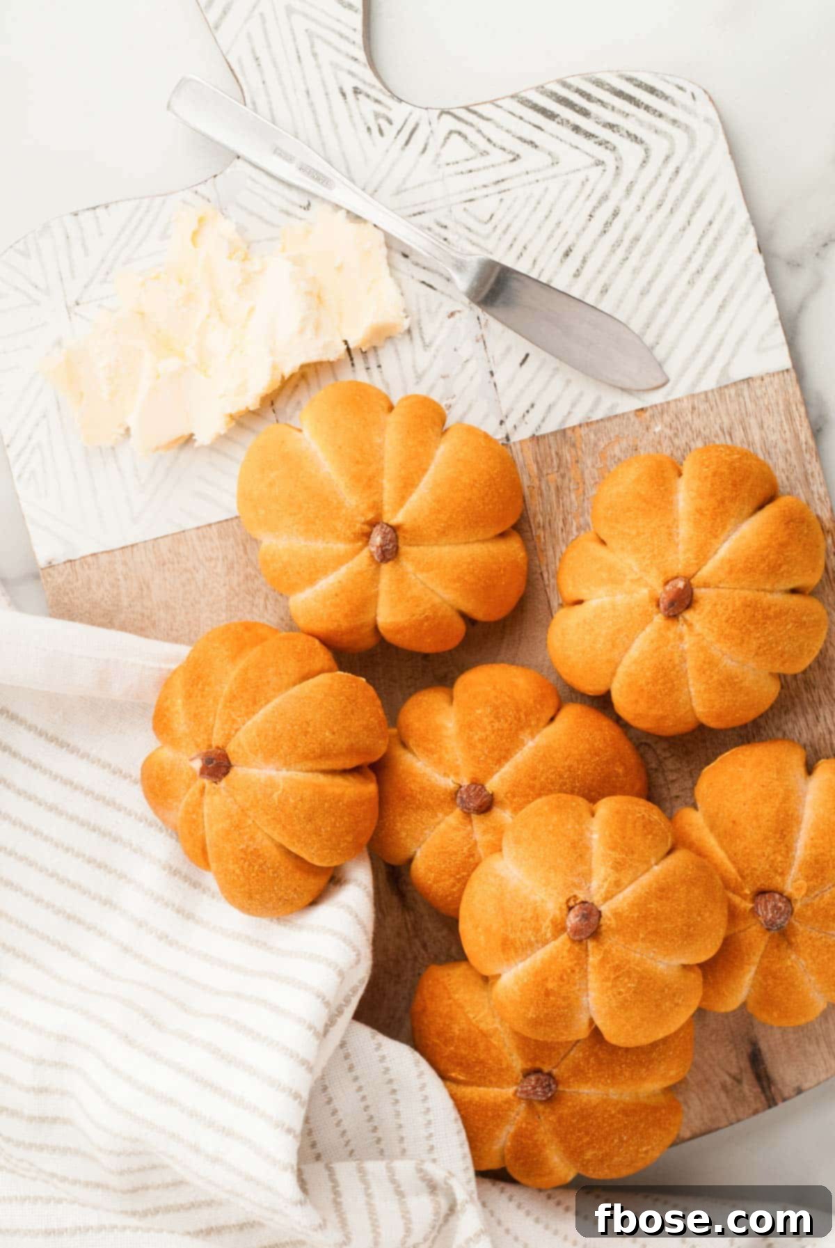 Spiced Pumpkin Feast Rolls 4 Overhead view of perfectly baked pumpkin dinner rolls arranged on a serving board with a knob of butter, ready to be enjoyed.