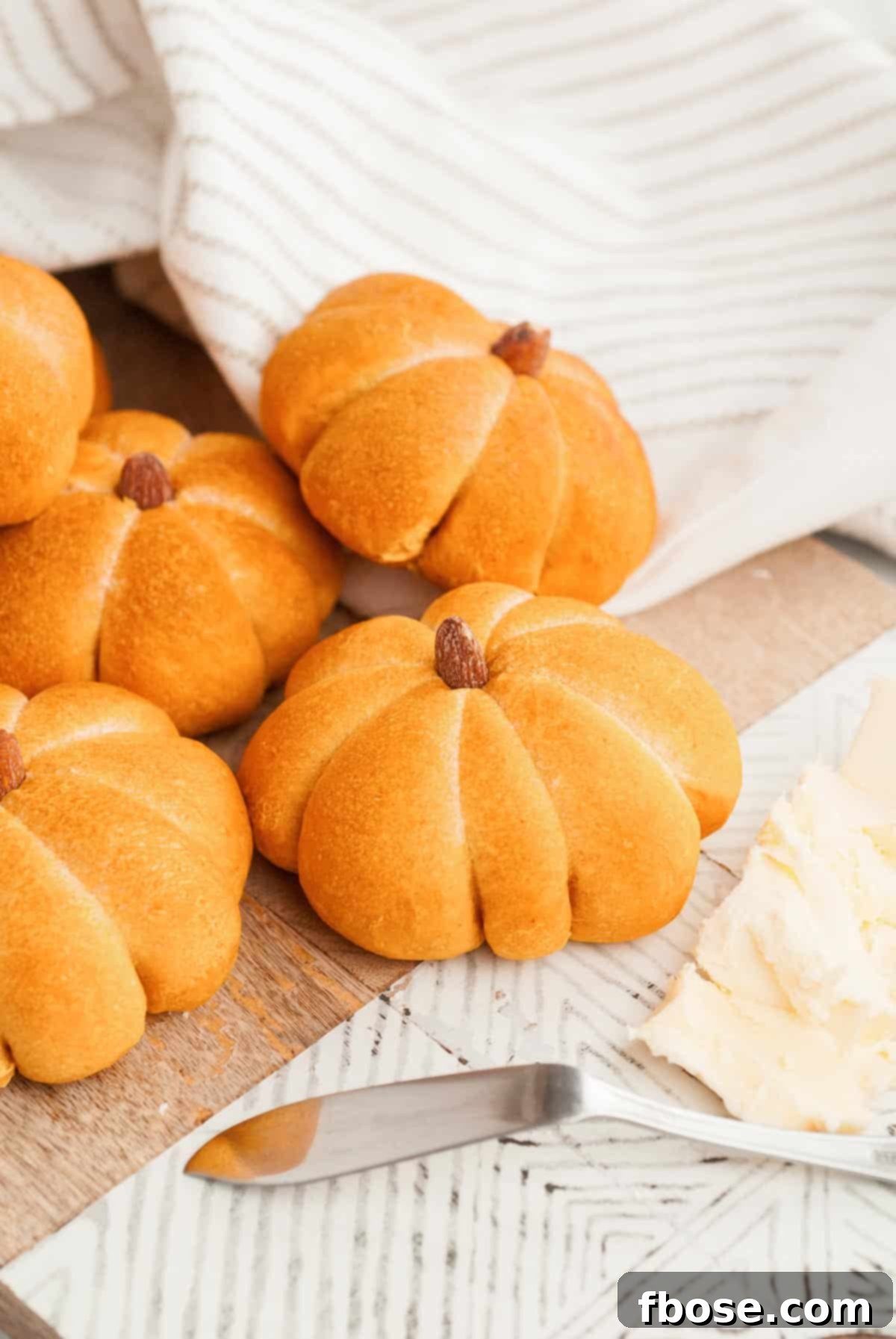 Spiced Pumpkin Feast Rolls 6 Pumpkin dinner rolls arranged on a serving board with a small dish of butter and a knife, ready for serving.
