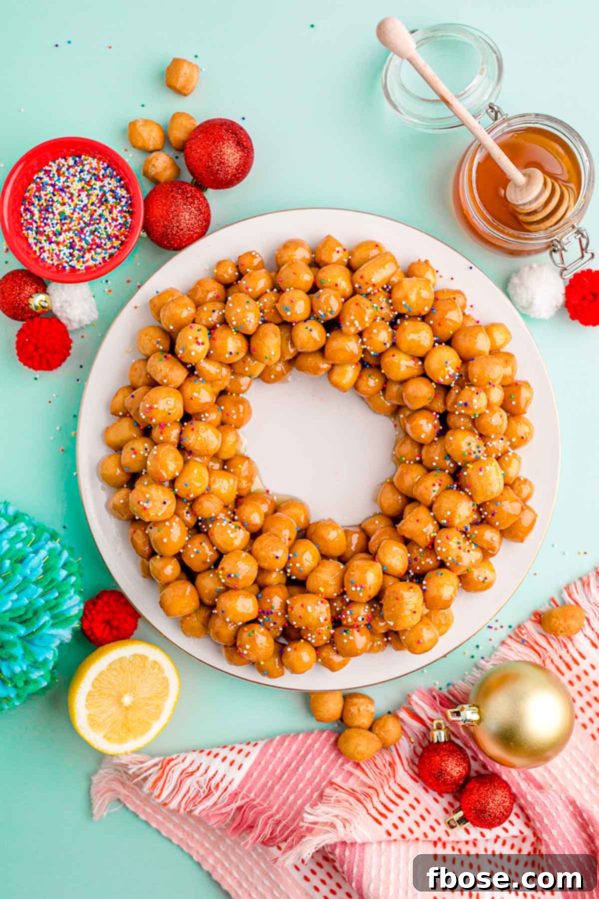 Classic Italian Struffoli 3 Overhead photo of struffoli on a white plate on a mint green surface with holiday decorations scattered around.