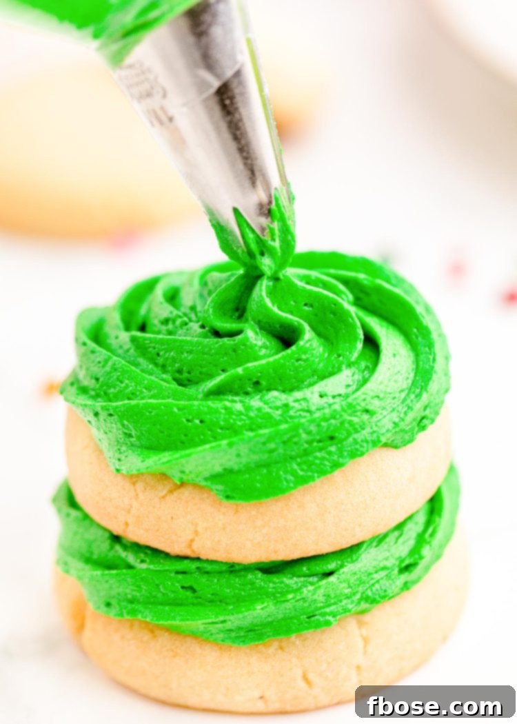 Festive Fir Tree Treats 11 Close up photo capturing the intricate process of stacking sugar cookies with rich green frosting, with the final top cookie in the process of being piped with icing, creating a Christmas tree.