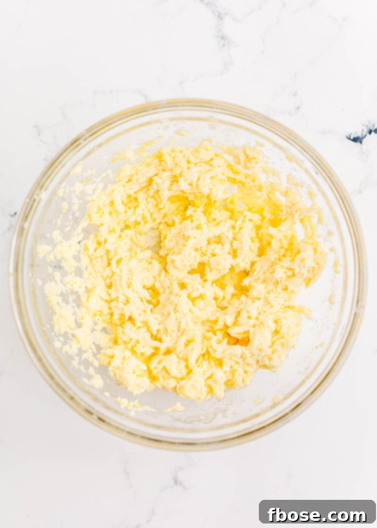 Festive Fir Tree Treats 5 Softened butter and granulated sugar perfectly creamed together in a clear glass mixing bowl, resting on an elegant marble surface, ready for the next step of the recipe.