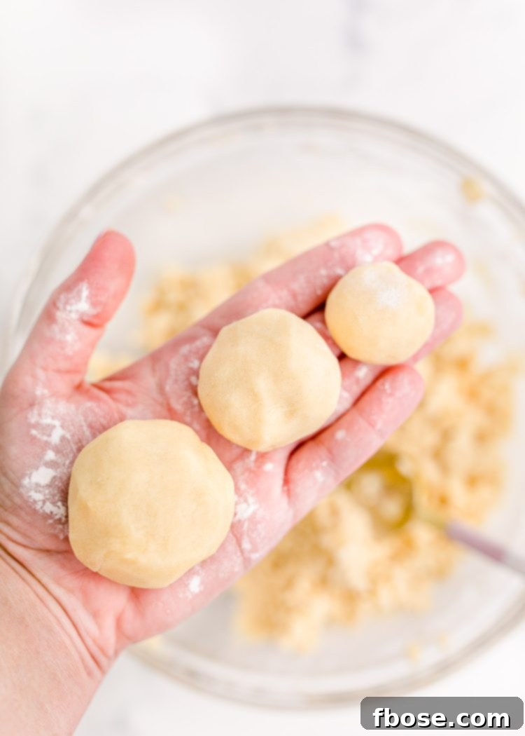 Festive Fir Tree Treats 7 A woman's hand delicately holding three distinct sizes of sugar cookie dough balls, illustrating the tiers for the Christmas tree cookie stacks.