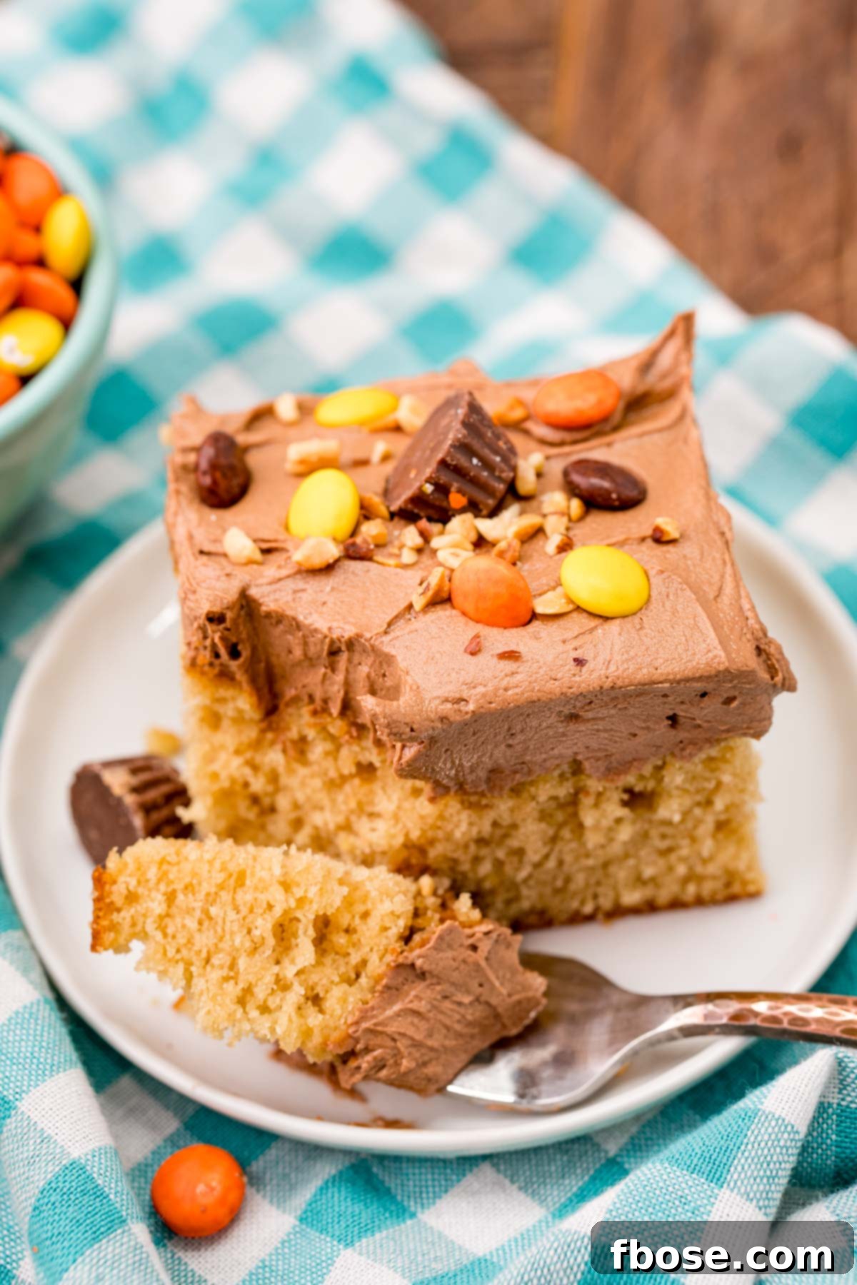 Ultimate Peanut Butter Sheet Cake 6 A slice of peanut butter cake on a white plate with a fork taking a bite out of it.
