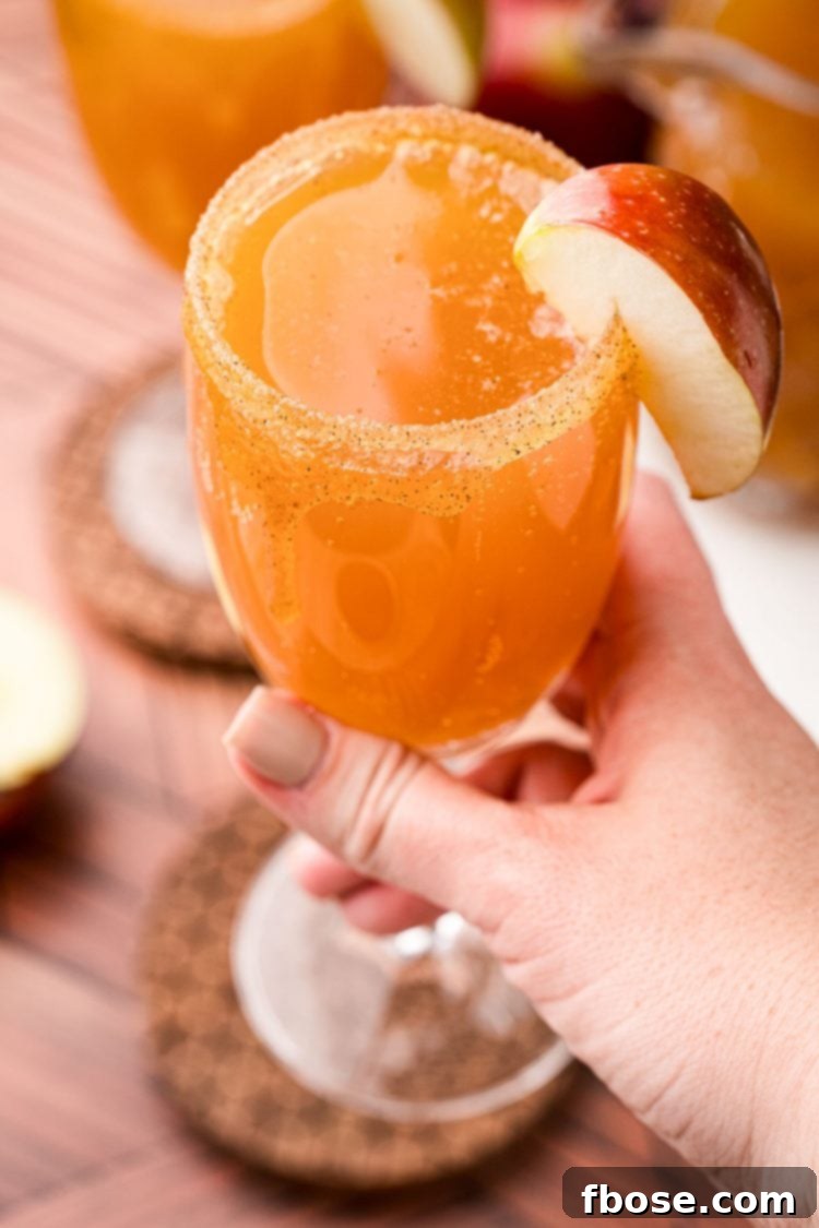 A woman's hand holding an apple cider mimosa close to the camera.