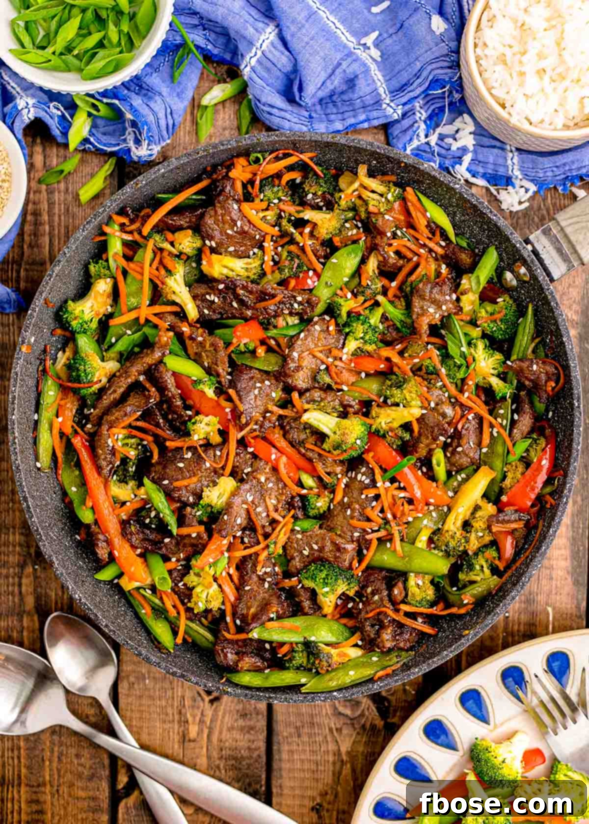 Overhead photo of a pan with beef stir fry in it on a wooden table with blue napkin next to it.