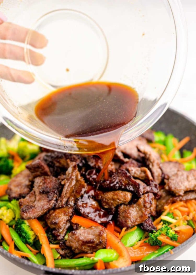 Sauce being poured over beef stir fry in a skillet.