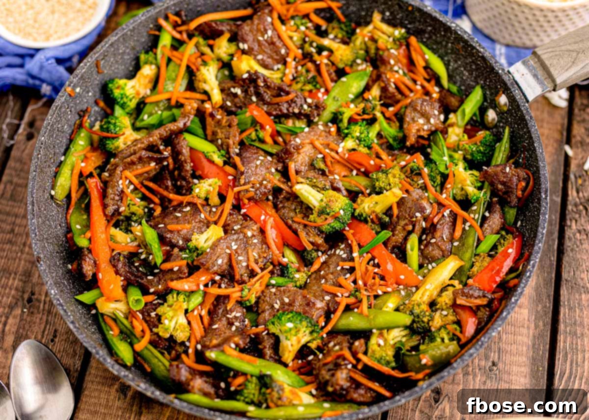 Overhead photo of a pan with beef stir fry in it on a wooden table with blue napkin next to it.