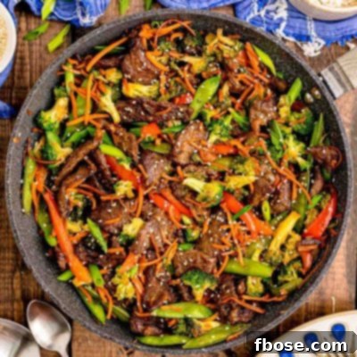 Overhead photo of a pan with beef stir fry in it on a wooden table with blue napkin next to it.