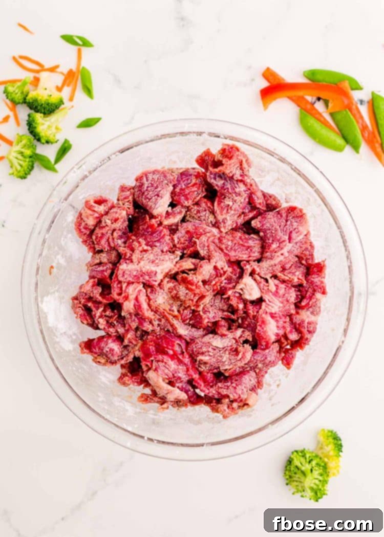 Thin strips of flank steak in a bowl on a marble counter.
