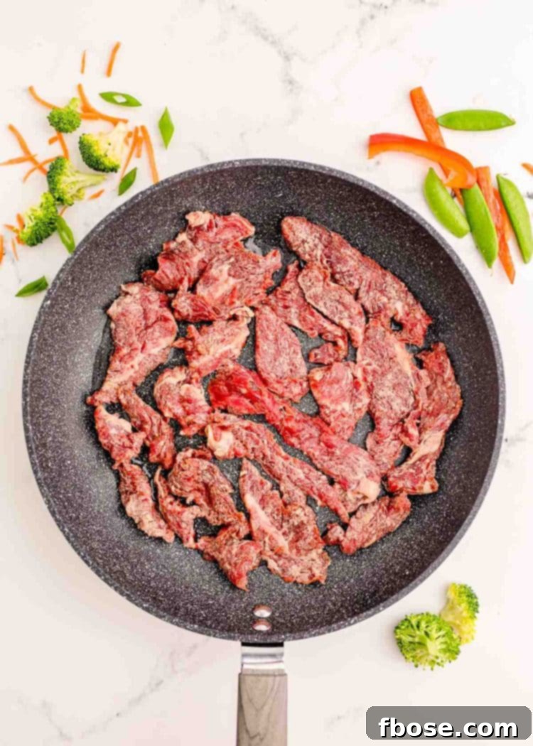 Strips of flank steak being fried in a skillet.