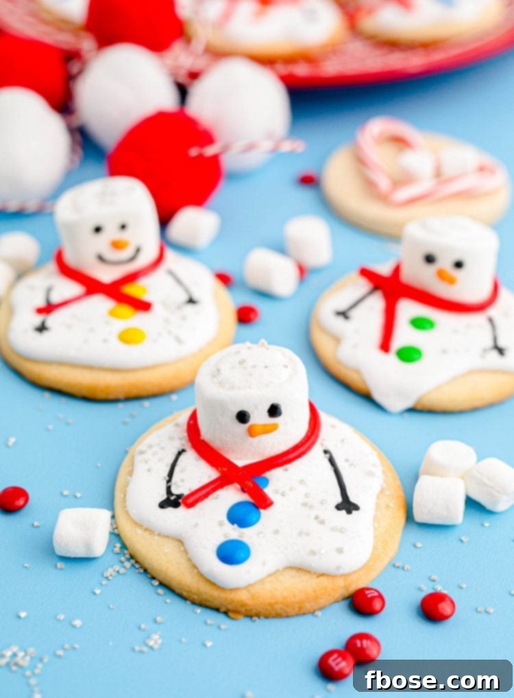Melty Snowman Cookies 7 Melted Snowman Cookies on a blue surface with candy and marshmallows scattered around, ready for decorating.