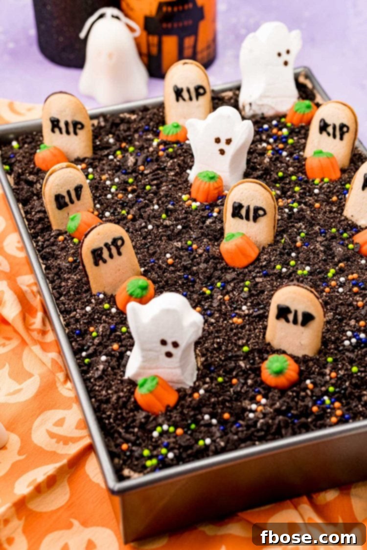 Halloween graveyard dirt cake in a 9x13-inch pan on an orange napkin, featuring tombstones and ghost decorations.
