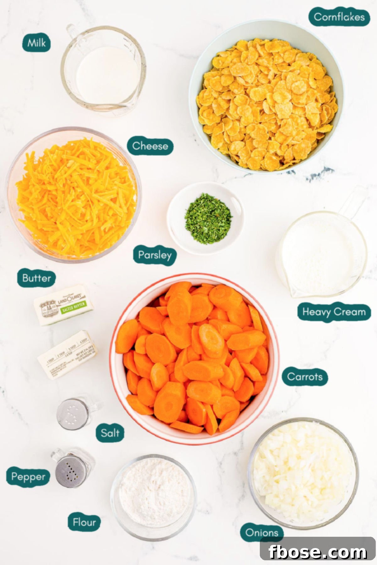 Overhead photo of ingredients prepared to make carrot casserole on a marble table, including fresh carrots, cheese, milk, and cornflakes.