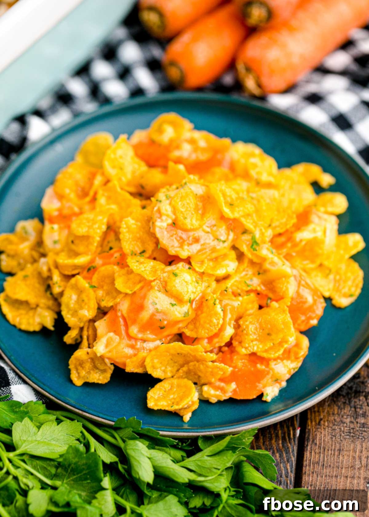 Close up photo of carrot casserole on a blue plate on a black and white checkered napkin with carrots and parsley on the side of the plate. Highlighted texture and freshness.