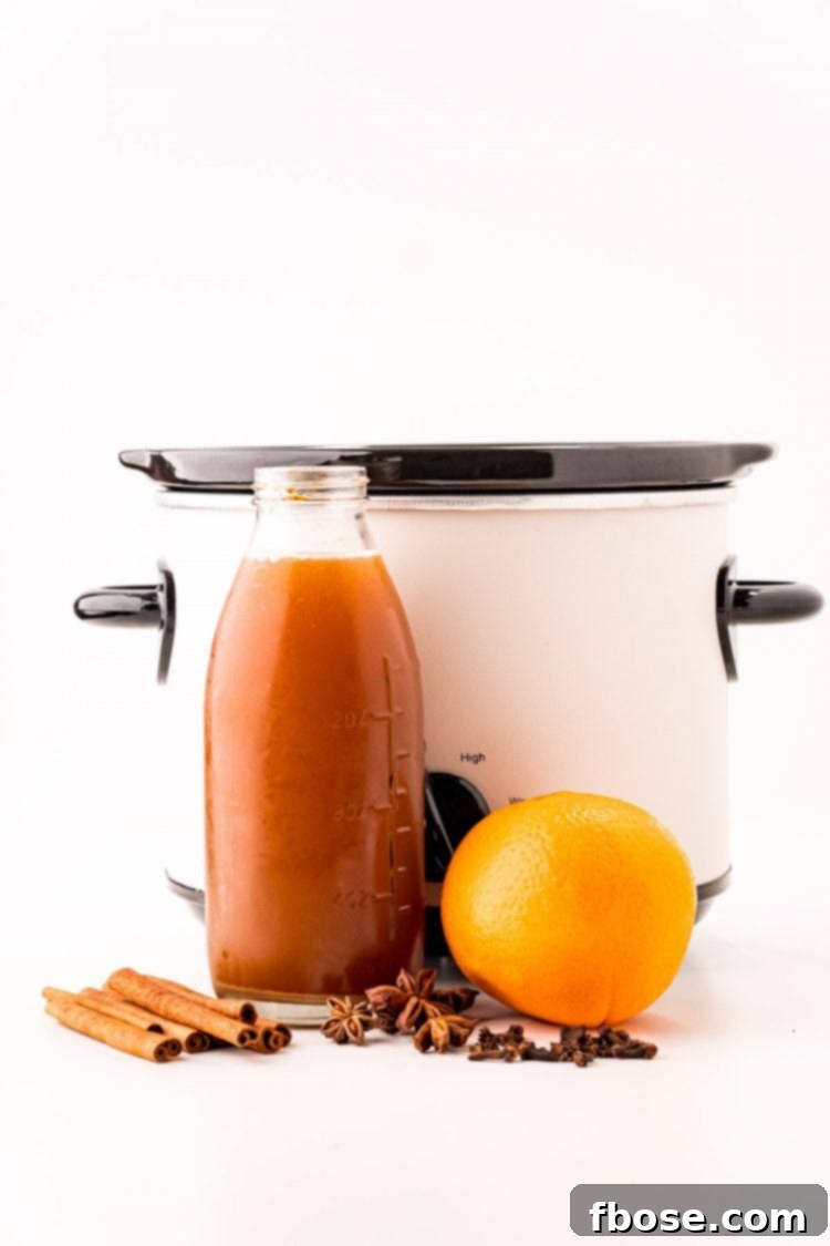 Ingredients to make mulled apple cider in front of a white crockpot on a white counter.