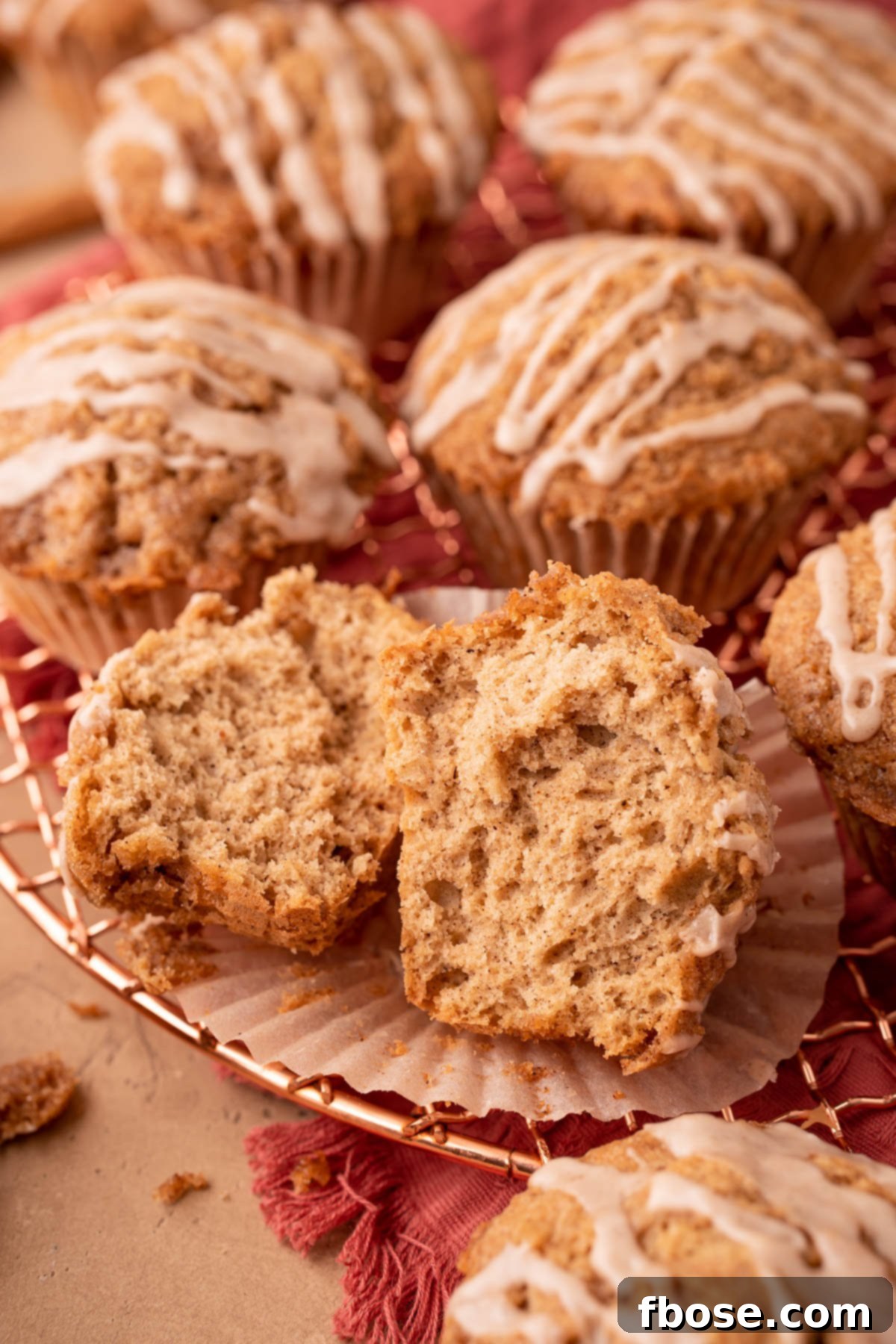 A perfectly baked vanilla chai muffin split open, revealing its tender, spiced interior, resting on a copper wire rack with other muffins.