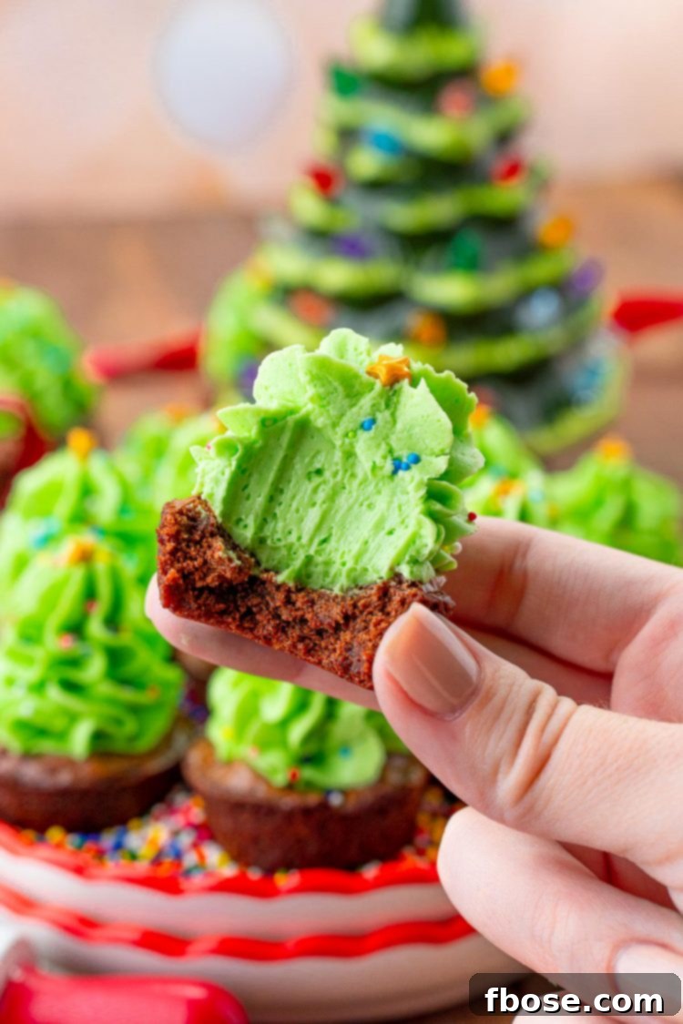 A woman's hand holding a christmas tree brownie bite that has a bite taken out of it. 