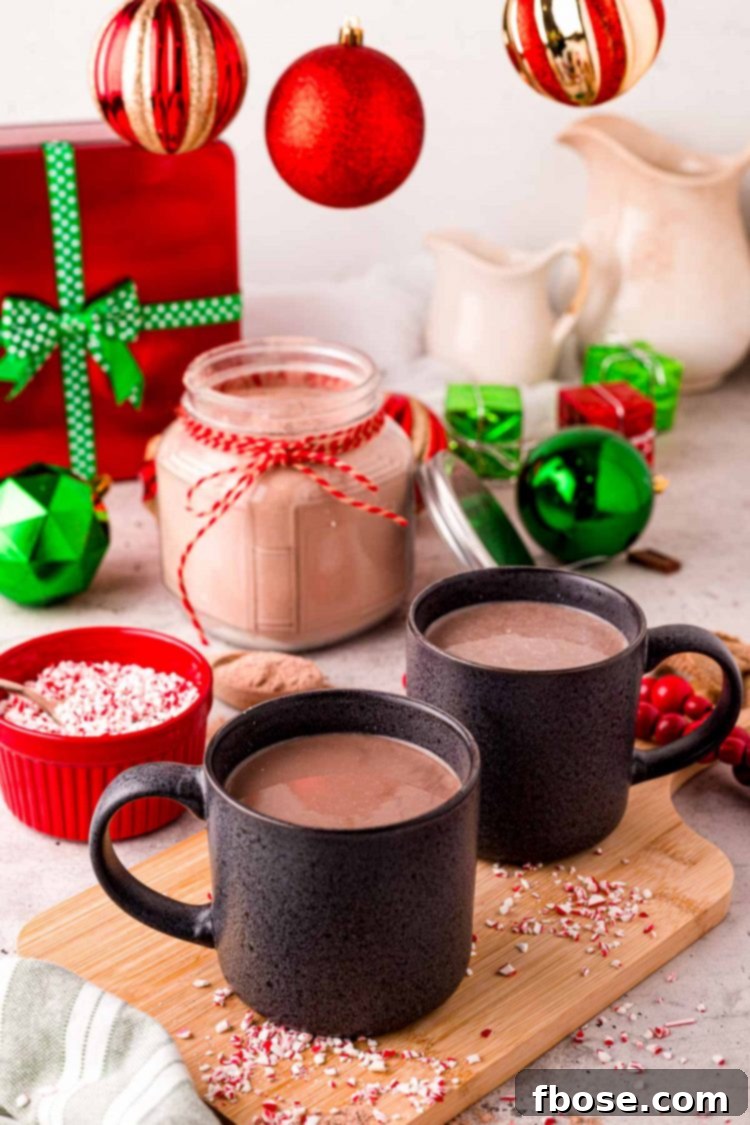 Two black mugs filed with hot chocolate one a wooden cutting board with holiday decorations in the back.