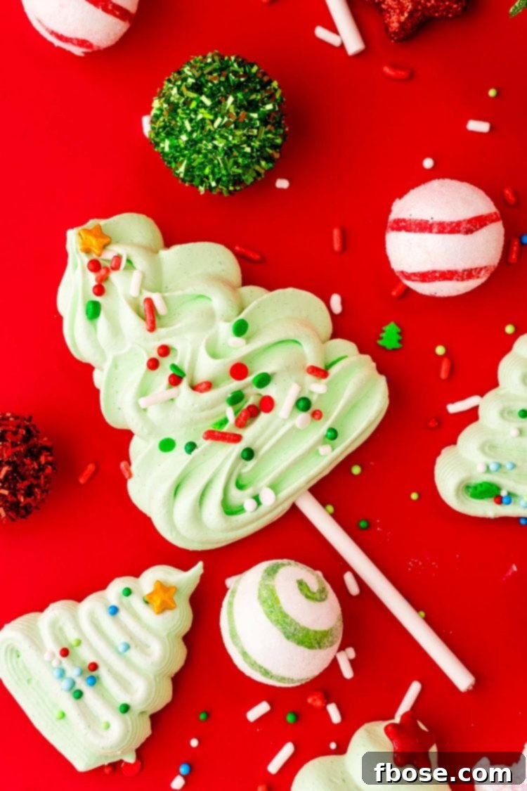 Christmas Tree Mernigue cookies and cookie pops on a red surface surrounded by sprinkles and holiday decor.