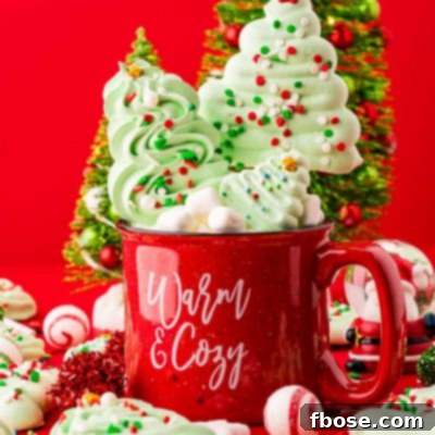 Close up photo of meringue christmas tree cookies and pops in and around a red holiday mug with decorative trees in the background.