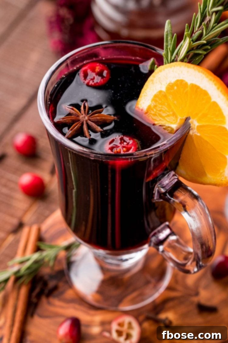 Close up photo of a glass mug filled with mulled wine garnished with rosemary and orange slice.