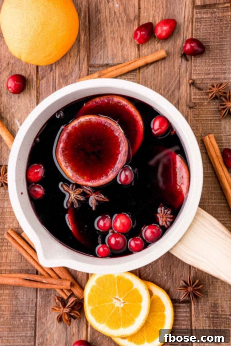 Overhead photo of mulled wine in a small light colored pot with spices and orange slices around it.