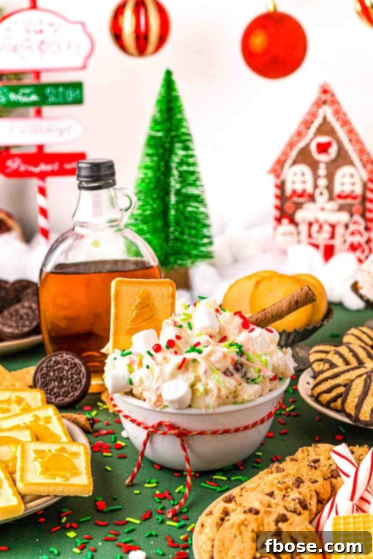Close up photo of a white bowl filled with Christmas dessert dip with cookies around it on a green surface.