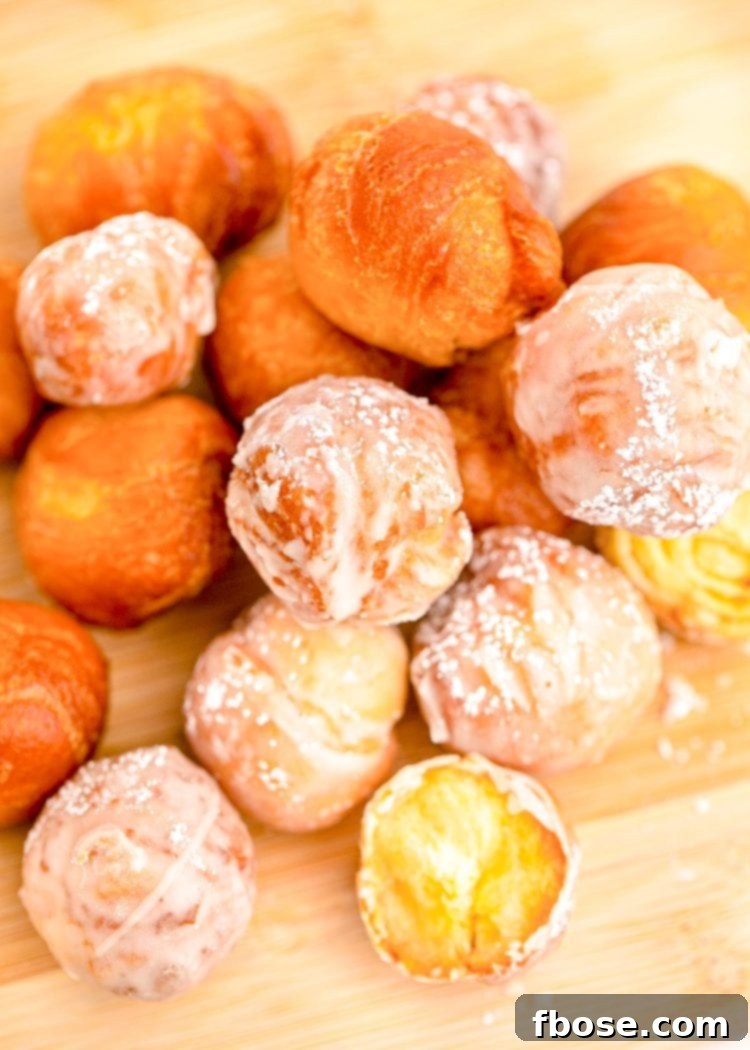 Close up photo of fried donut holes on a wooden cutting board, glistening with glaze.