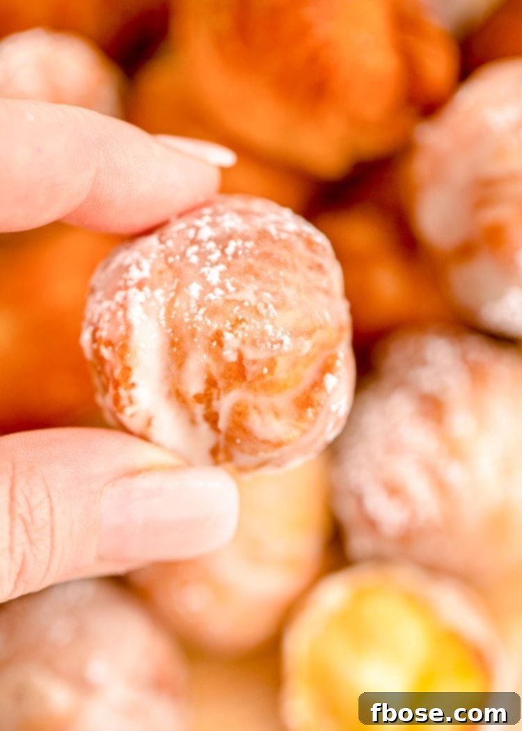 A woman's hand holding a donut hole over a plate with more donut holes, showcasing the soft interior.