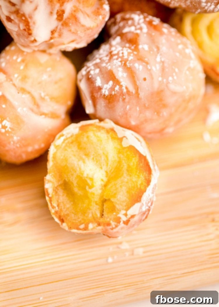 Donut holes on a wooden cutting board with the closest one missing a bite, showing the fluffy interior.