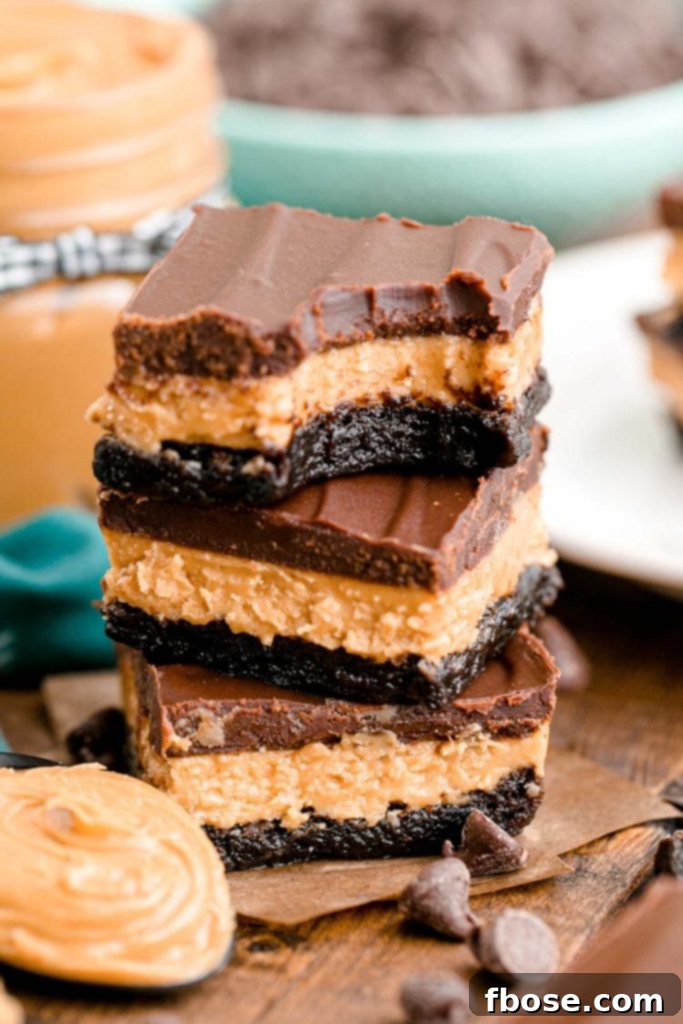 Buckeye Bliss Brownies 2 Close up photo of a stack of three buckeye brownies on a wooden table with chocolate chips and peanut butter around it.