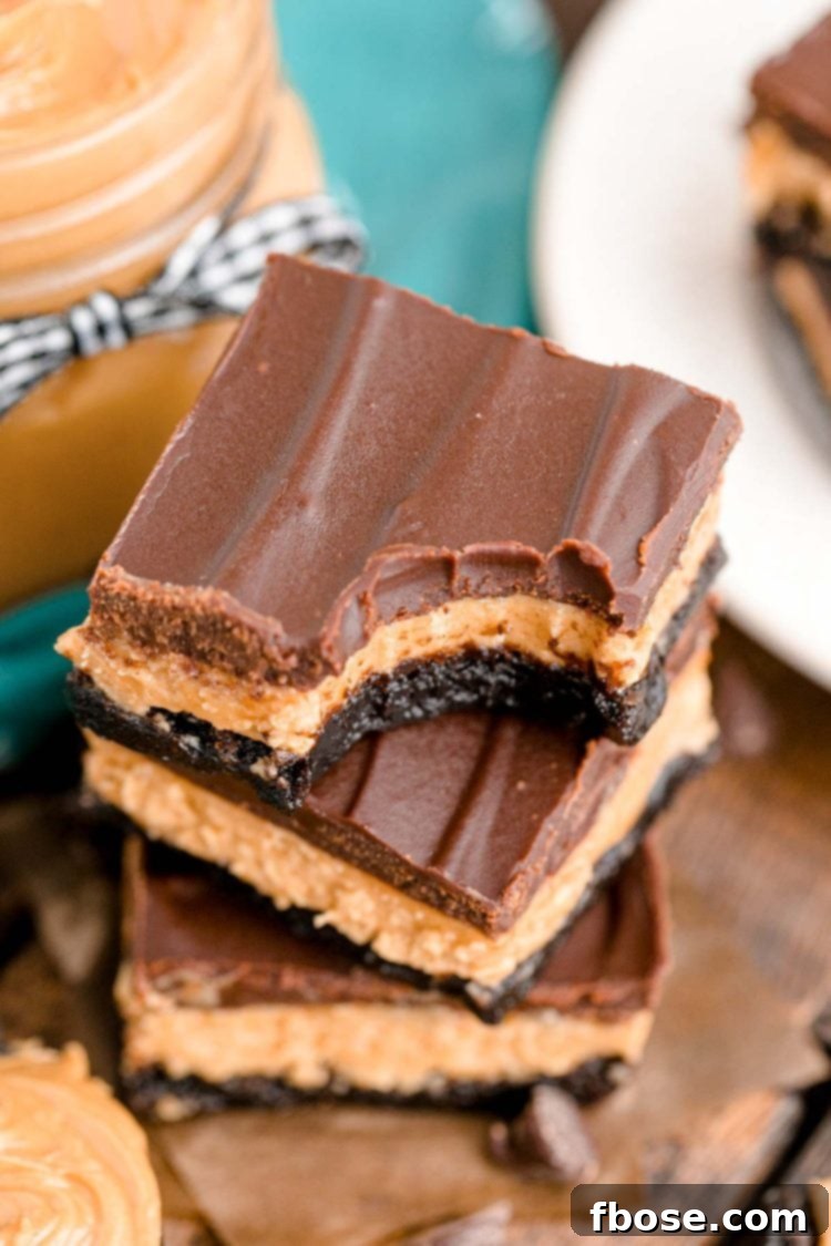 Buckeye Bliss Brownies 3 Close up photo of a stack of three buckeye brownies on a wooden table with chocolate chips and peanut butter around it.