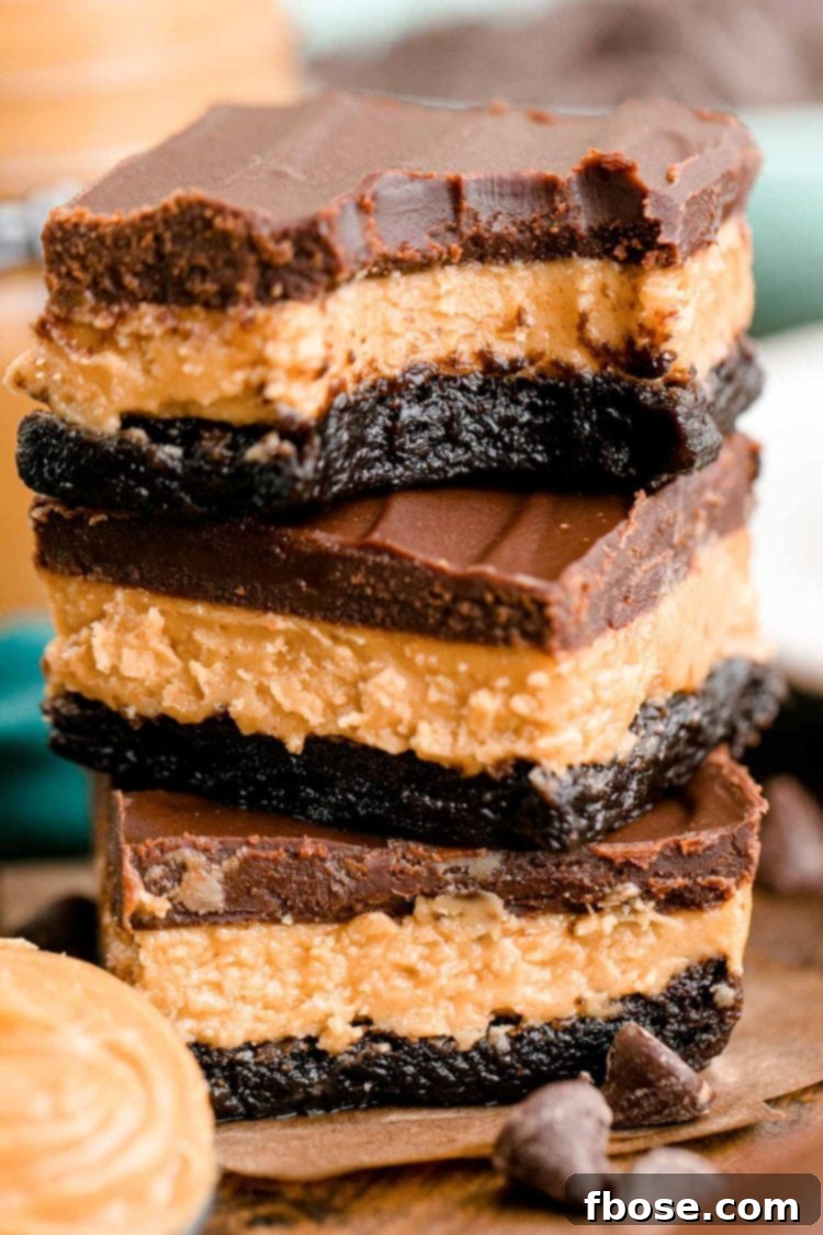 Buckeye Bliss Brownies 6 Close up photo of a stack of three buckeye brownies on a wooden table with chocolate chips and peanut butter around it.