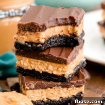 Buckeye Bliss Brownies 7 Close up photo of a stack of three buckeye brownies on a wooden table with chocolate chips and peanut butter around it.