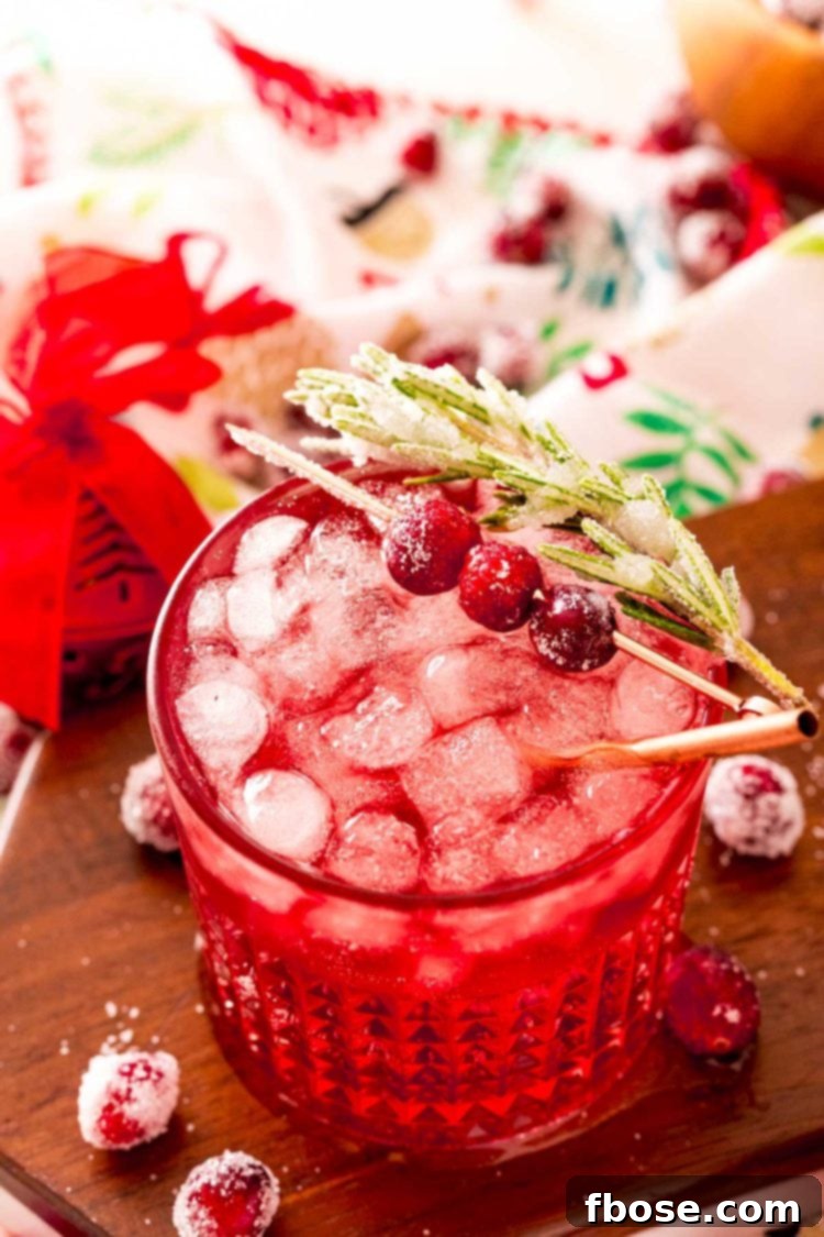 Close up photo of a sparkling vodka cranberry cocktail on a wooden board with holiday decor around it.