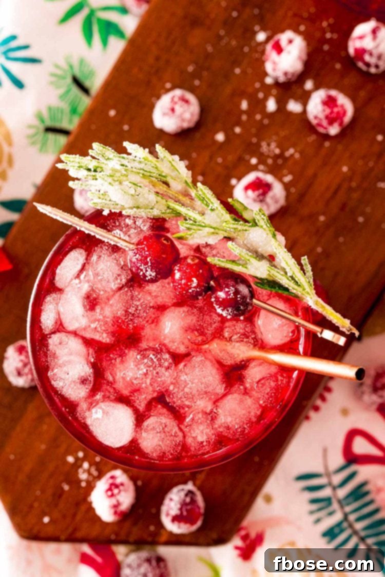 Close up photo of a sparkling vodka cranberry cocktail on a wooden board with holiday decor around it.
