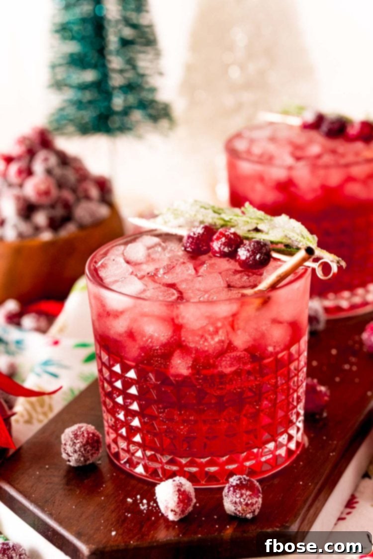 Close up photo of a sparkling vodka cranberry cocktail on a wooden board with holiday decor around it.