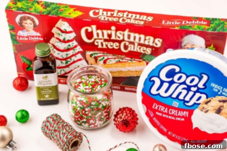 All ingredients used to make Christmas tree cake dip laid out on a clean white table, including Little Debbie Christmas Tree Cakes, Cool Whip, vanilla extract, and festive sprinkles.