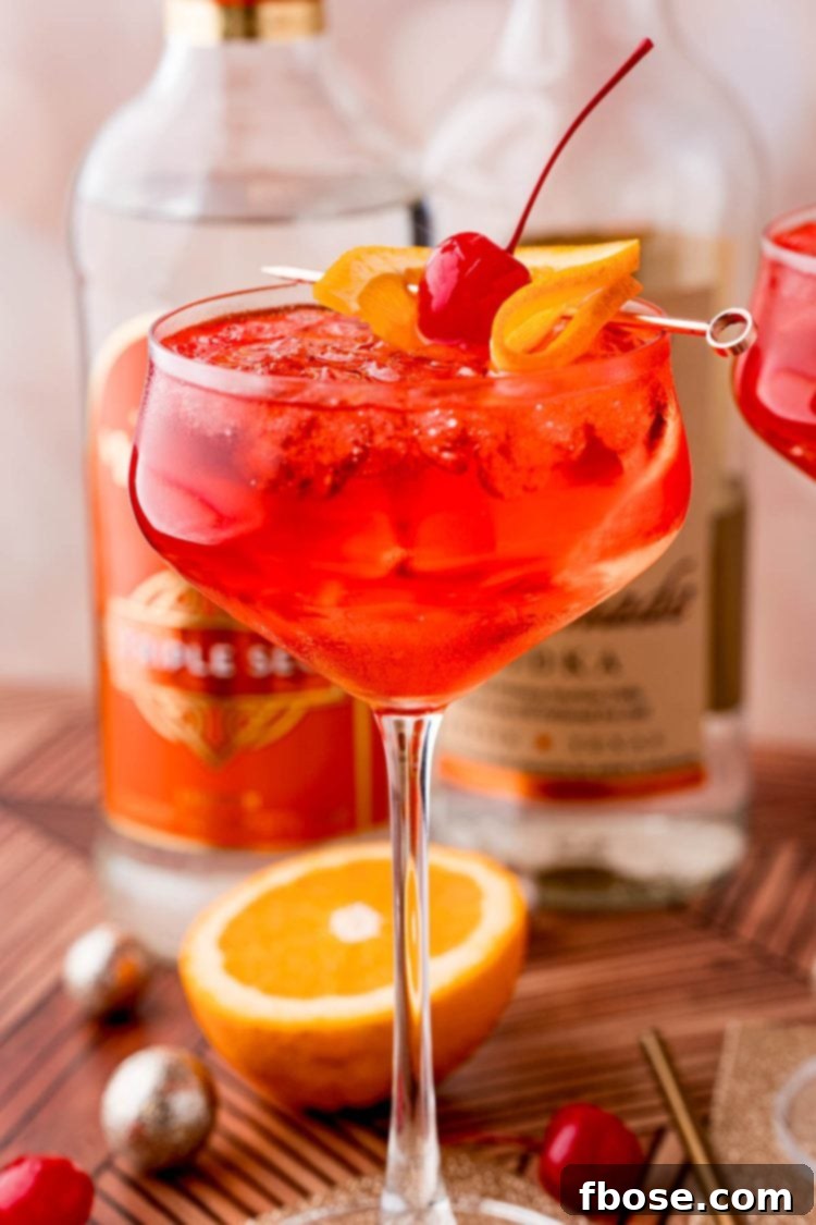 Close up photo of a dirty shirley drink in a cocktail glass on a gold coaster with maraschino cherries, oranges and decorations scattered around.