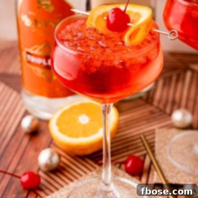 Close up photo of a dirty shirley drink in a cocktail glass on a gold coaster with maraschino cherries, oranges and decorations scattered around.