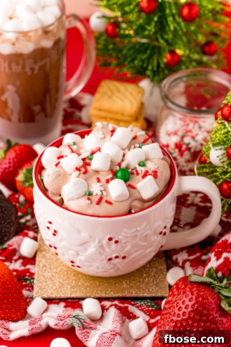 Close up photo of a white holiday mug filled with hot chocolate dip with marshmallows and sprinkles on top. 