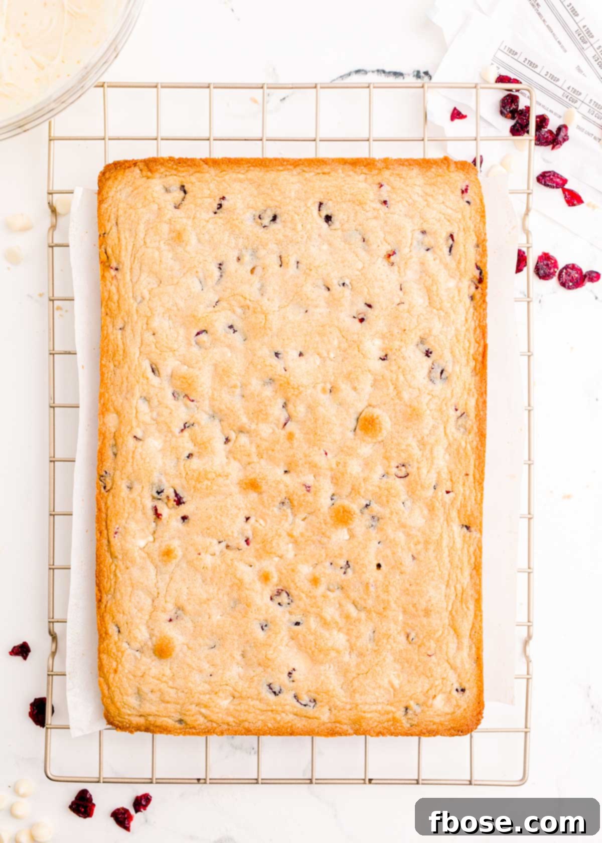Freshly baked cranberry bliss bars, golden and delicious, are cooling on a wire rack, filling the air with a sweet aroma.