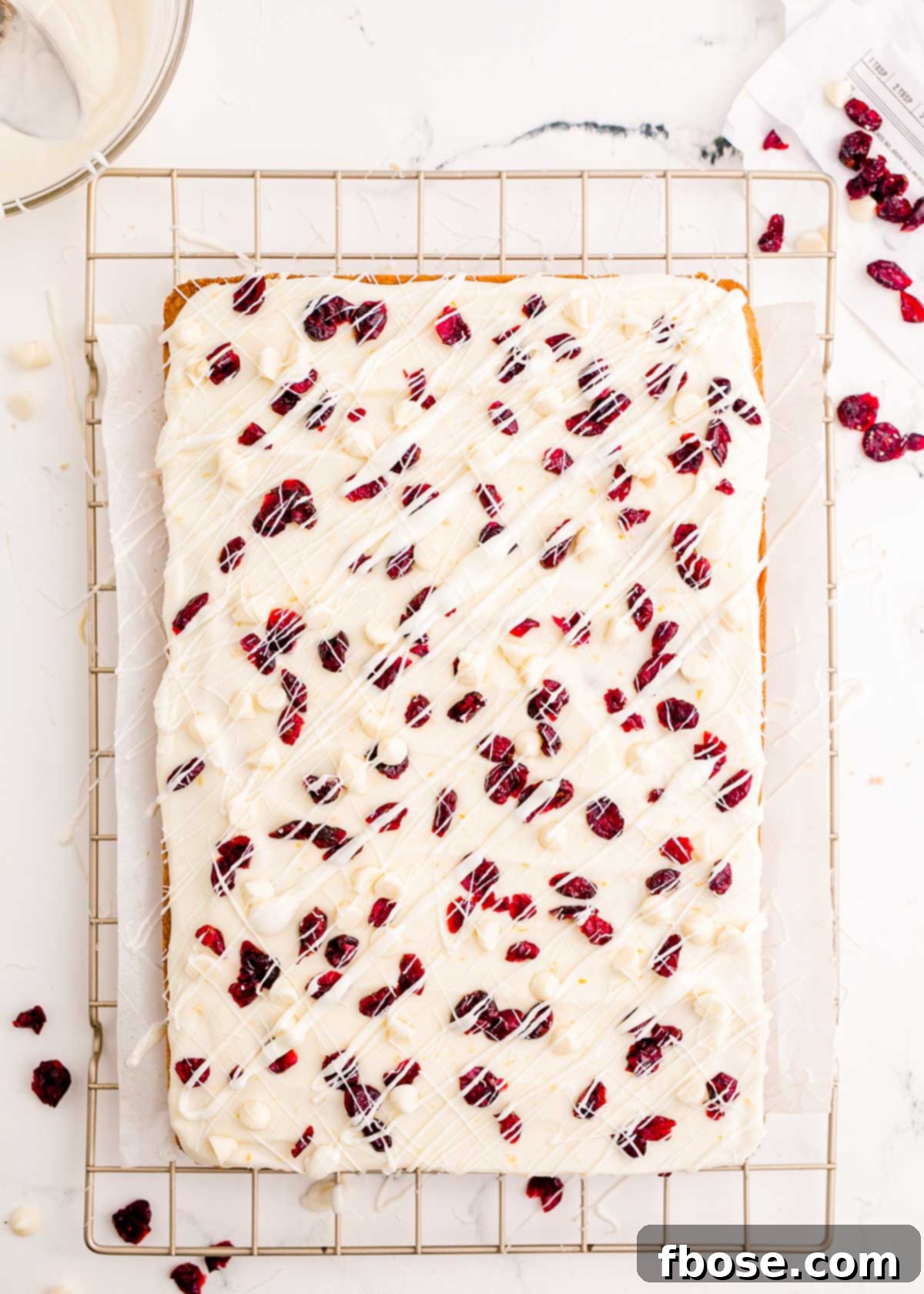 A pristine tray of uncut cranberry bliss bars, beautifully frosted and drizzled, cooling on a wire rack, ready for slicing and serving.