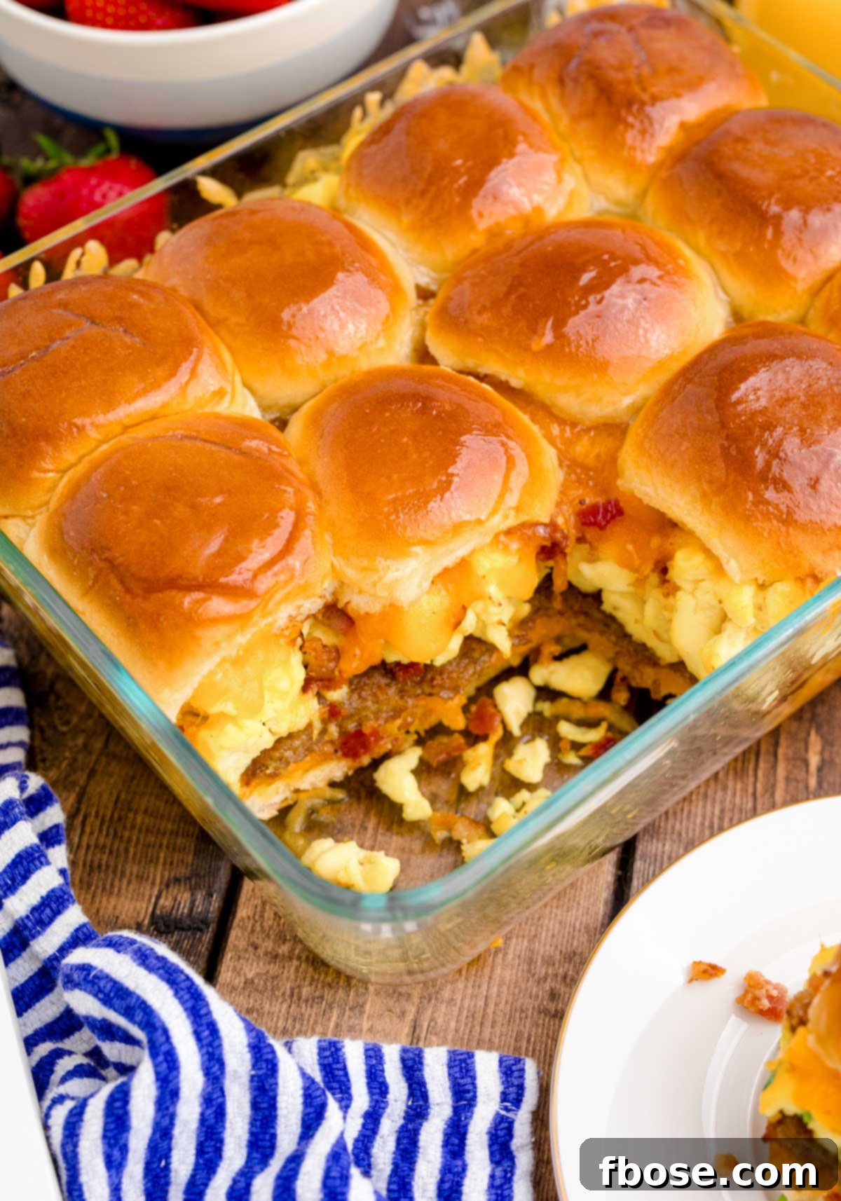 A baking dish of breakfast sliders on a wooden table on a blue and white striped napkin.