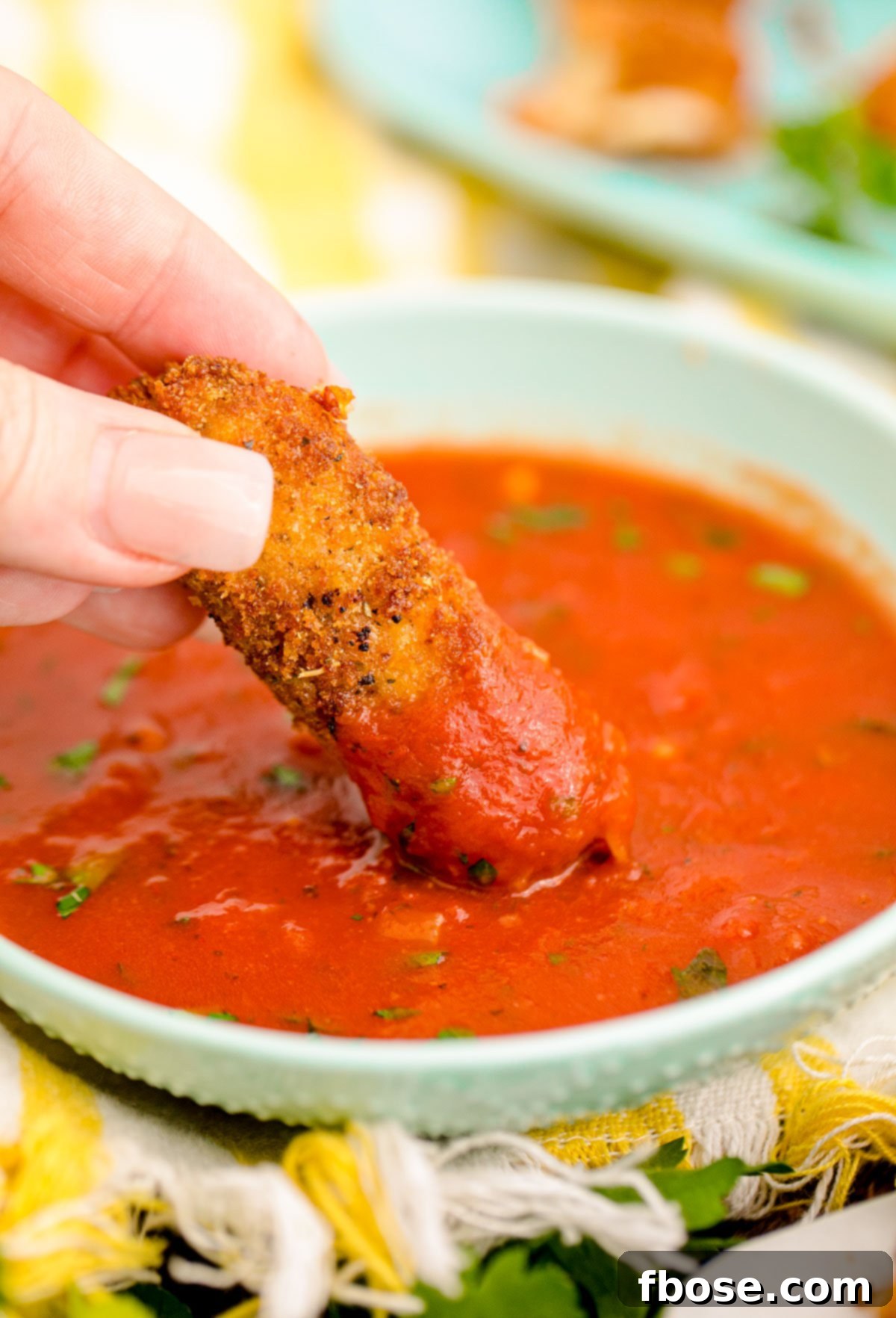 Mozzarella sticks being dipped in marinara sauce.