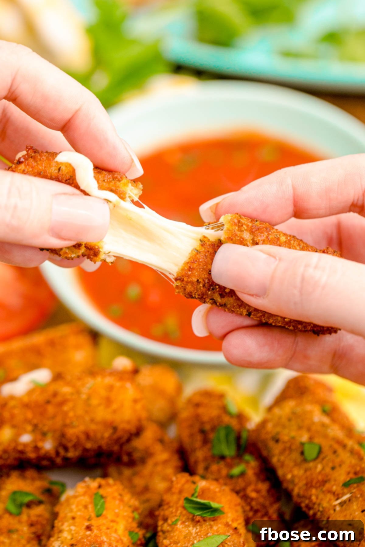 A woman's hand pulling a mozzarella stick apart. 