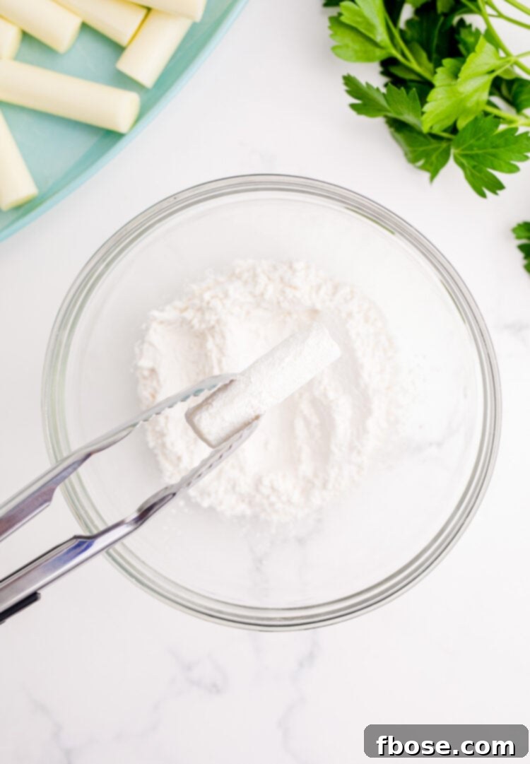 A piece of cheese stick being dipped in flour.