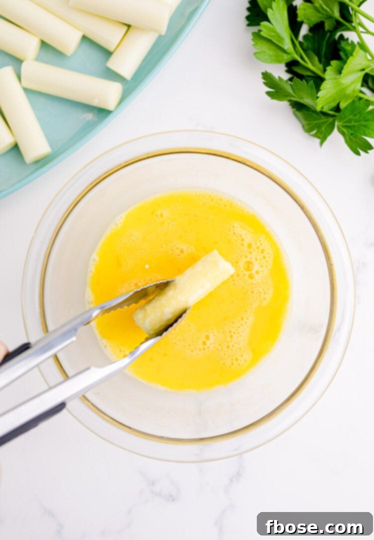 Cheese sticks being dipped in egg wash with tongs.