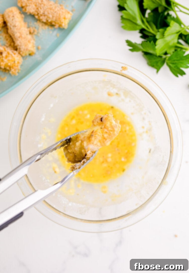 Tongs dipping mozzarella sticks in an eggwash.
